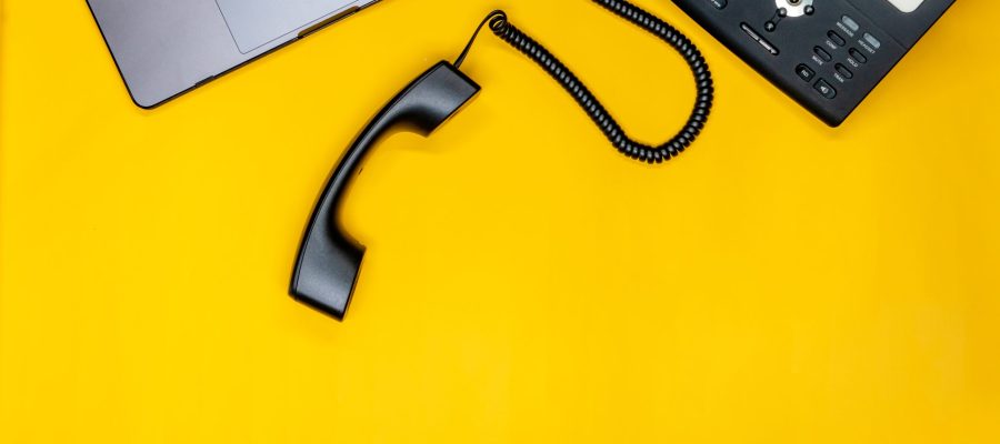 Office telephone receiver and laptop on yellow desk background symbolizing contact communication